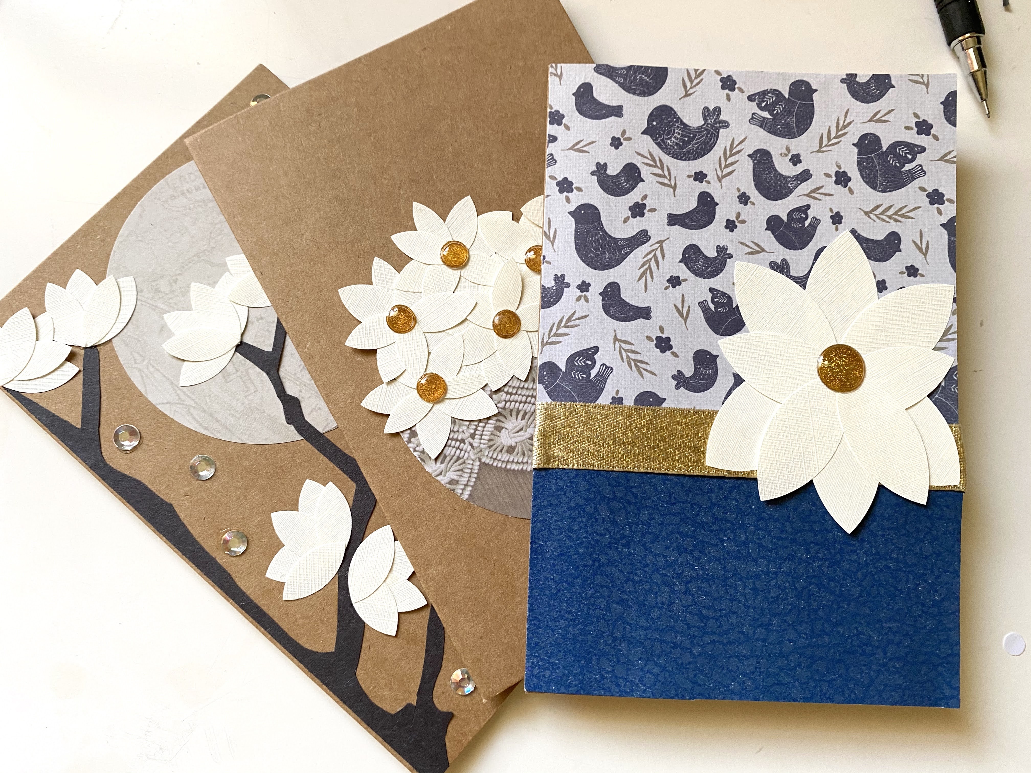 A set of homemade magnolia flower cards made from paper, ribbons, rhinestones, and glittered dots.